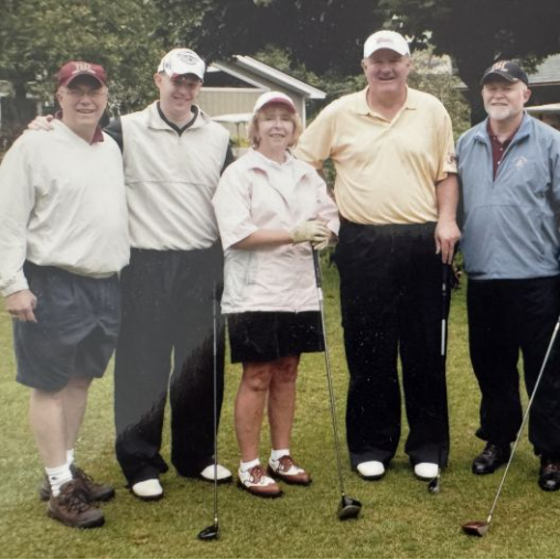 Six golfers pose with clubs on a grassy course near golf carts.